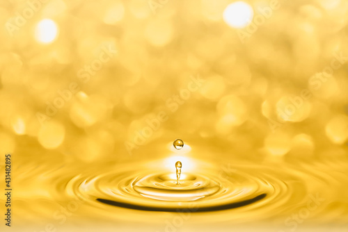 Macro photography of a droplets splash of golden liquid shining and creating circular waves on a bright sparkles bokeh background.