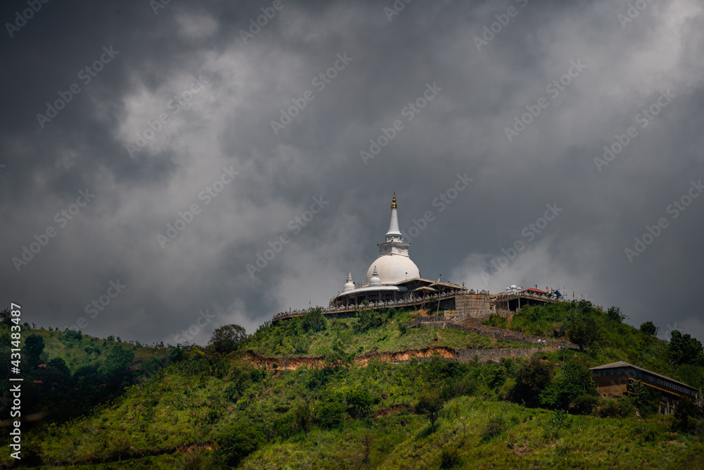 Mahamevnawa Buddhist Monastery temple in the mountain top low angle scenic landscape view. dark rainy clouds and cold atmosphere in Bandarawela, stupa glowing brightly in the distant hill. Mahamevnawa Buddhist Monastery temple in the mountain top low angle scenic landscape view. dark rainy clouds and cold atmosphere in Bandarawela, stupa glowing brightly in the distant hill.