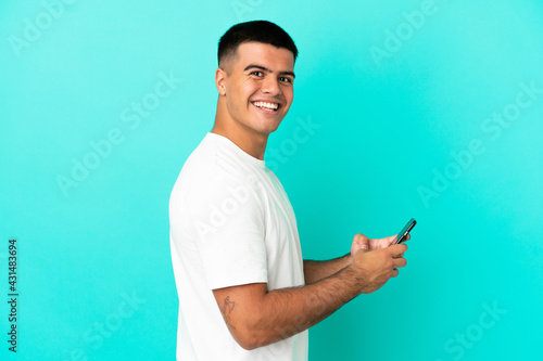 Young handsome man over isolated blue background sending a message or email with the mobile