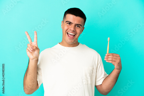 Young handsome man brushing teeth over isolated blue background smiling and showing victory sign