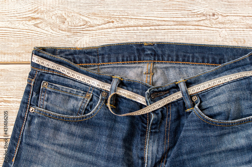 Measuring tape for weight loss in jeans on a wooden background. The concept of being overweight. Selective focus.