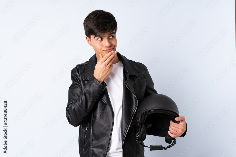 Man with a motorcycle helmet over isolated blue background thinking an idea Man with a motorcycle helmet over isolated blue background thinking an idea