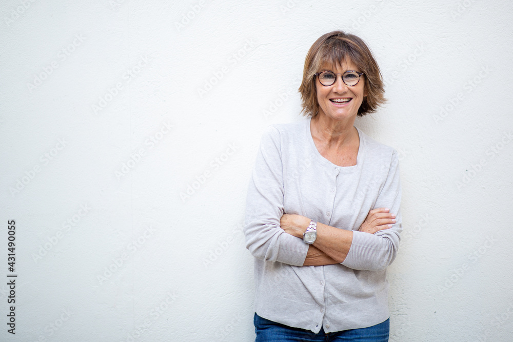 smiling older woman with arms crossed by white background smiling older woman with arms crossed by white background