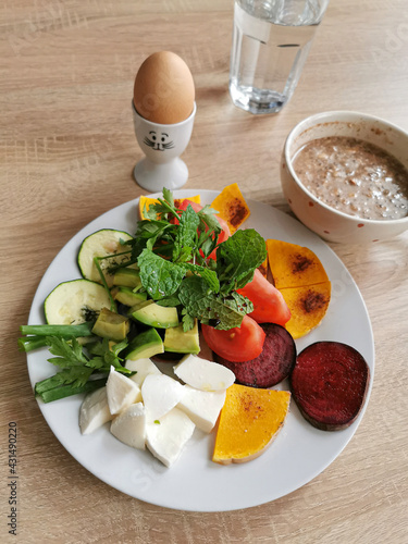 A healthy breakfast rich in protein, fats and carbohydrates.
Oatmeal with nuts, soft-boiled egg, mocarella cheese, colorful vegetables, green leaves of mint, parsley and onion photo