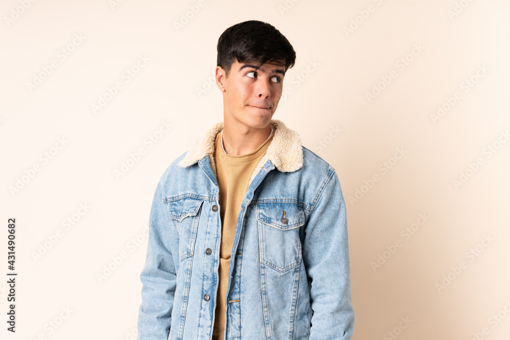 Handsome man over isolated beige background having doubts while looking up Handsome man over isolated beige background having doubts while looking up