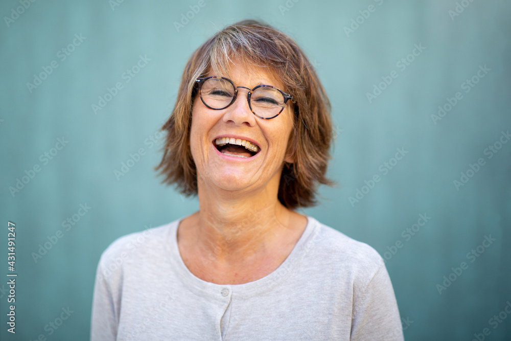 Close up woman in 50s laughing by green background Close up woman in 50s laughing by green background