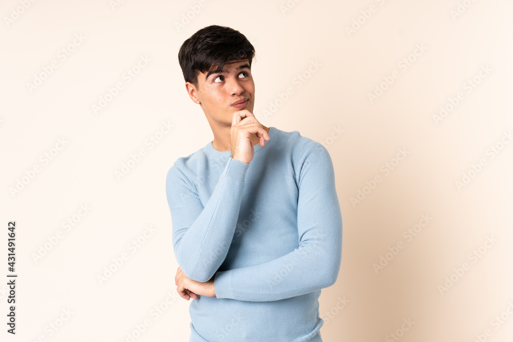 Handsome man over isolated beige background and looking up Handsome man over isolated beige background and looking up
