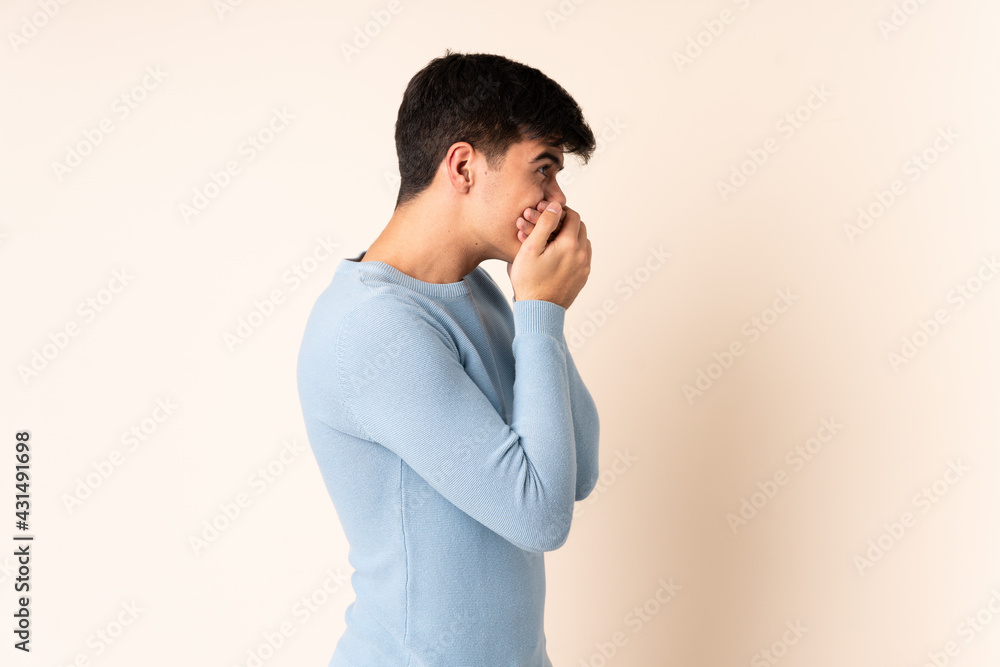 Handsome man over isolated beige background covering mouth and looking to the side Handsome man over isolated beige background covering mouth and looking to the side