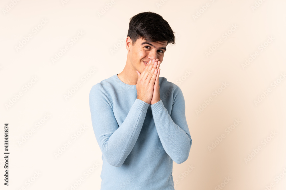 Handsome man over isolated beige background keeps palm together. Person asks for something Handsome man over isolated beige background keeps palm together. Person asks for something