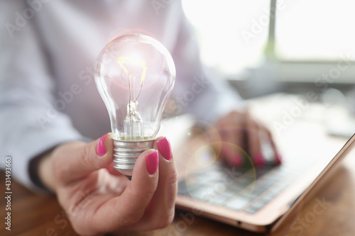 Woman typing on laptop keyboard and light bulb in hand closeup