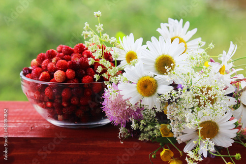 A glass bowl with strawberry and a daisy bouquet