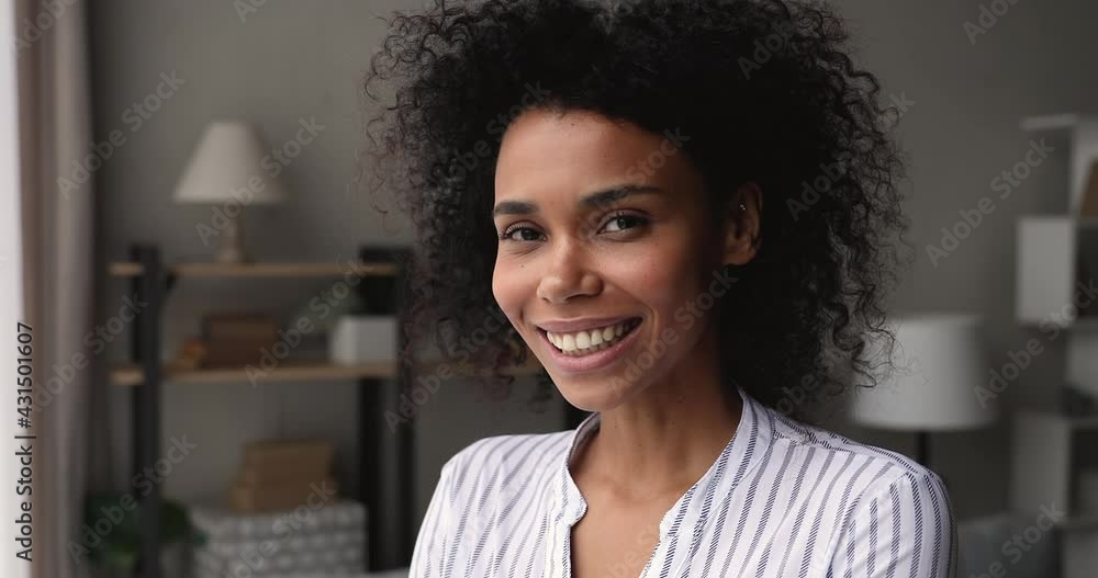 Head shot close up 35s African woman standing in living room daydreams look into distance. Female homeowner pose indoor looks at camera feels happy. Tenant, independent business lady portrait concept Head shot close up 35s African woman standing in living room daydreams look into distance. Female homeowner pose indoor looks at camera feels happy. Tenant, independent business lady portrait concept