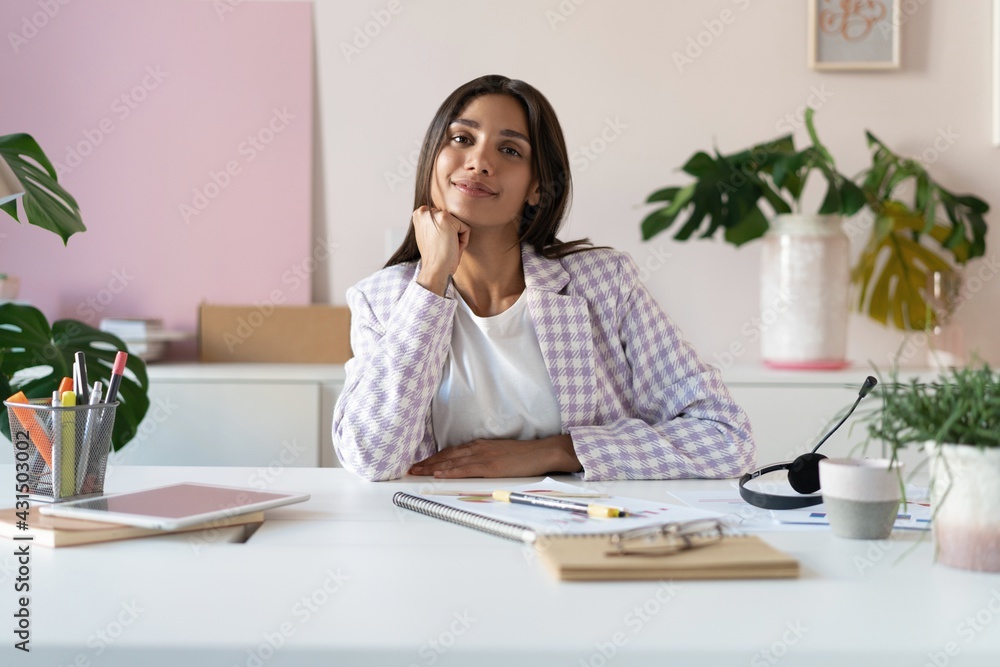 Portrait of a cheerful Indian mixed-race businesswoman sitting at the table in office and looking at camera. Portrait of a cheerful Indian mixed-race businesswoman sitting at the table in office and looking at camera.
