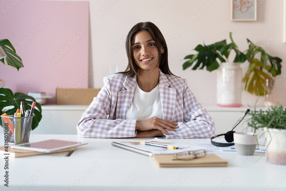 Portrait of a cheerful Indian mixed-race businesswoman sitting at the table in office and looking at camera. Portrait of a cheerful Indian mixed-race businesswoman sitting at the table in office and looking at camera.