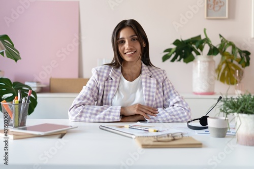 Portrait of a cheerful Indian mixed-race businesswoman sitting at the table in office and looking at camera.