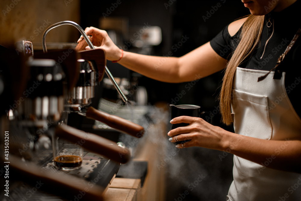 female barista turns on coffee machine that releases steam to make coffee drink