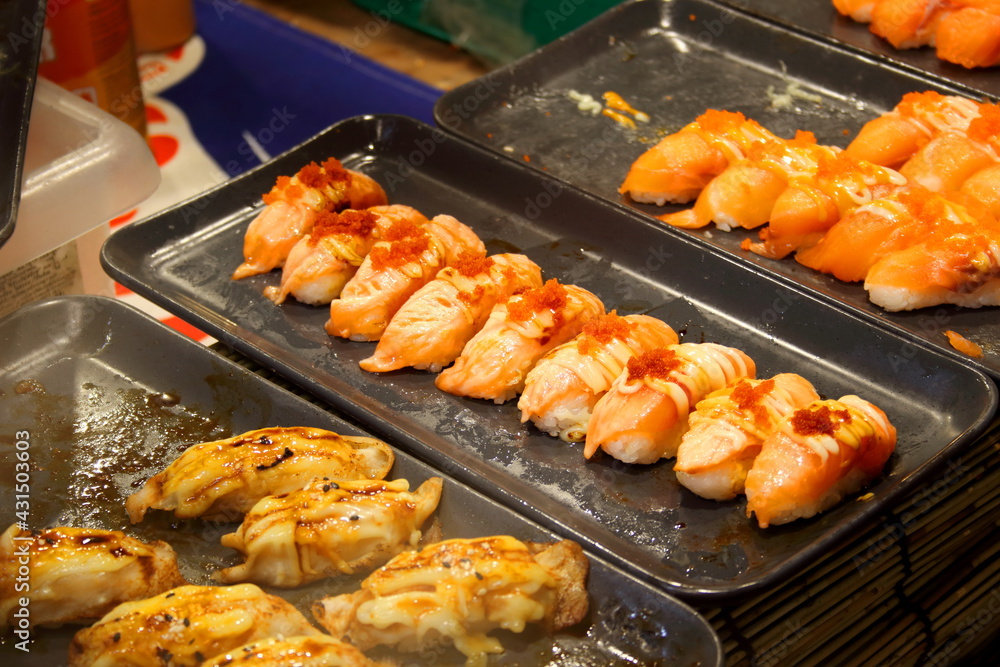 Sushi in row on black tray for sale, salmon grilled and mayonnaise on top, Thailand.