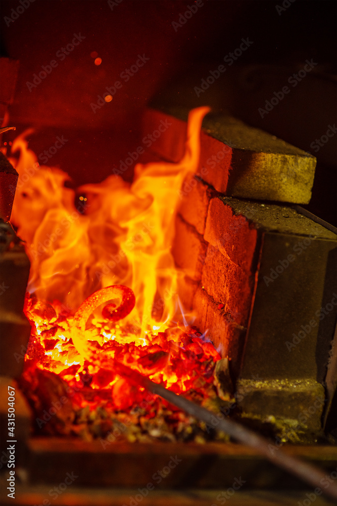 Fototapeta premium The metal spiral is heated to red in the forge in the forge during forging. Handicraft concept