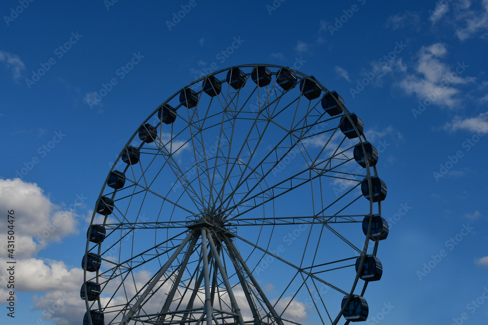 Part of the Ferris wheel with closed booths against a background of blue sky and clouds