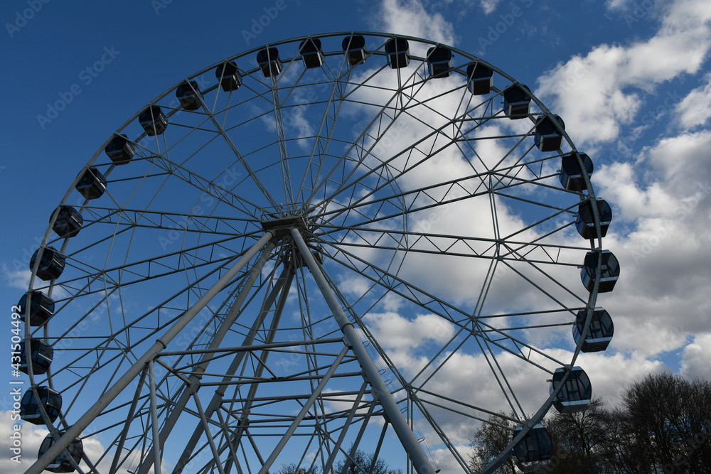 Part of the Ferris wheel with closed booths against a background of blue sky and clouds