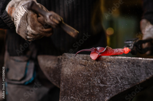 A close-up image of a blacksmith's hands forging a jewelry flower from a hot sheet of metal. Manual rework in the forge concept photo