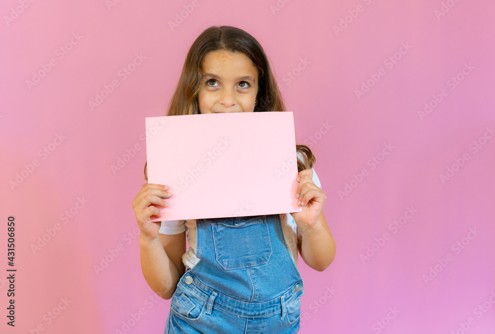 Smiling little girl holding empty pink board isolated over pink background. Smiling little girl holding empty pink board isolated over pink background.