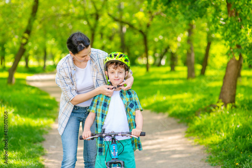 Mom hands out a bicycle helmet to a child standing with a bicycle in the summer in the park. Family Sports Vacation Concept