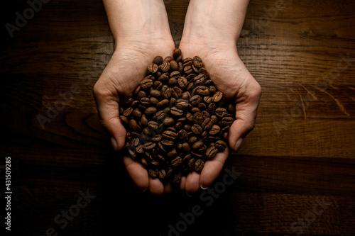 top view of hands accurate holding roasted aromatic coffee beans against background wooden surface