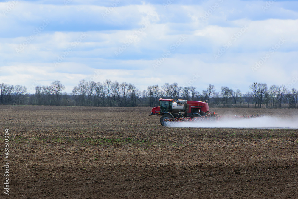 Red tractor with irrigation system watering a field on a cloudy day. agricultural machinery, work in the field. seasonal work. tractor fertilizes the ground Red tractor with irrigation system watering a field on a cloudy day. agricultural machinery, work in the field. seasonal work. tractor fertilizes the ground