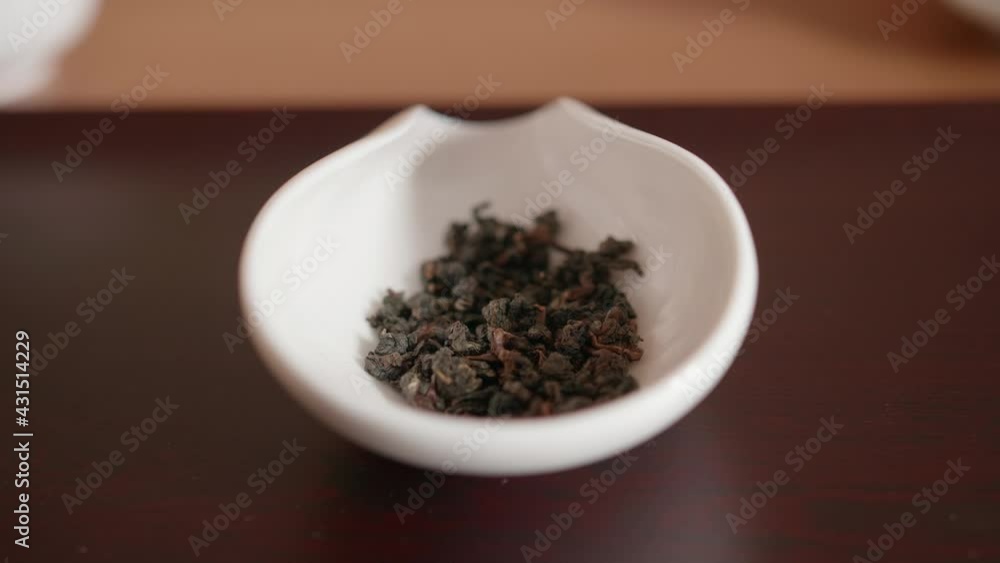 Dried rolled tea leaves dropping into a ceramic container, ready to be steeped Dried rolled tea leaves dropping into a ceramic container, ready to be steeped