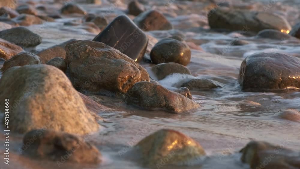 waves lap on a rocky beach with soft warm light with smooth pebble like rocks waves lap on a rocky beach with soft warm light with smooth pebble like rocks