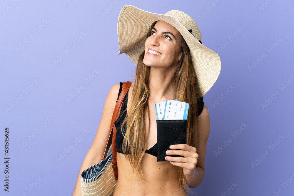 Young caucasian woman holding a passport for holidays isolated on purple background looking up while smiling Young caucasian woman holding a passport for holidays isolated on purple background looking up while smiling