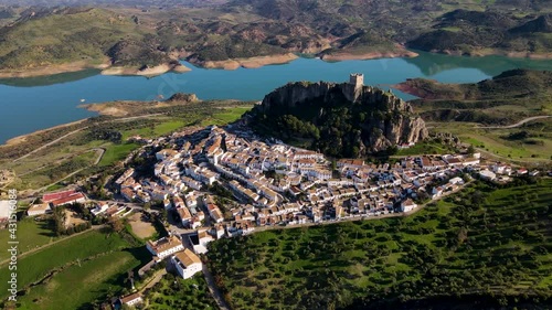 Flying towards the city of Zahara de la Sierra in Andalusia, Spain. The aerial shot reveals the old town overseen by a castle on top of the rock with a scenic lake in the background photo