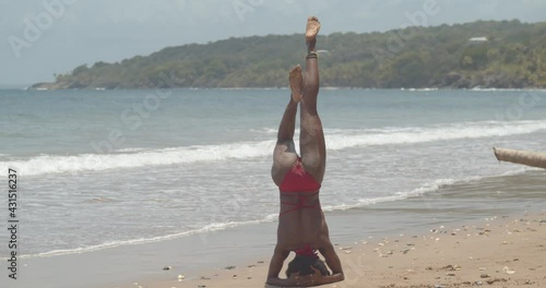 A contortionist in a hand stand position before dismounting into a pose with waves crashing the shoreline in the background photo