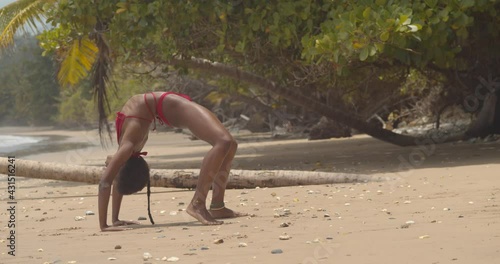 Contortionist coming out of a contortion pose while wearing a bikini at a beach location photo