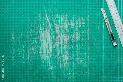 Old grunge green dirty cutting mat, with stainless steel ruler and cutter, grunge texture background,  top view of workspace, copy space for text and graphic.