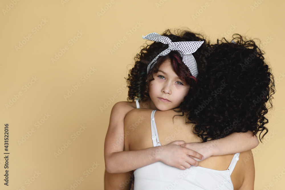 A little daughter looking through the shoulder of her mother on the beige background. A little daughter looking through the shoulder of her mother on the beige background.