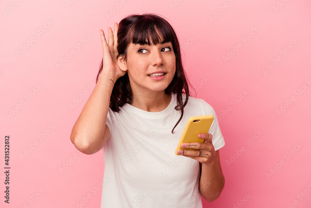 Young caucasian woman holding a mobile phone isolated on pink background trying to listening a gossip. Young caucasian woman holding a mobile phone isolated on pink background trying to listening a gossip.