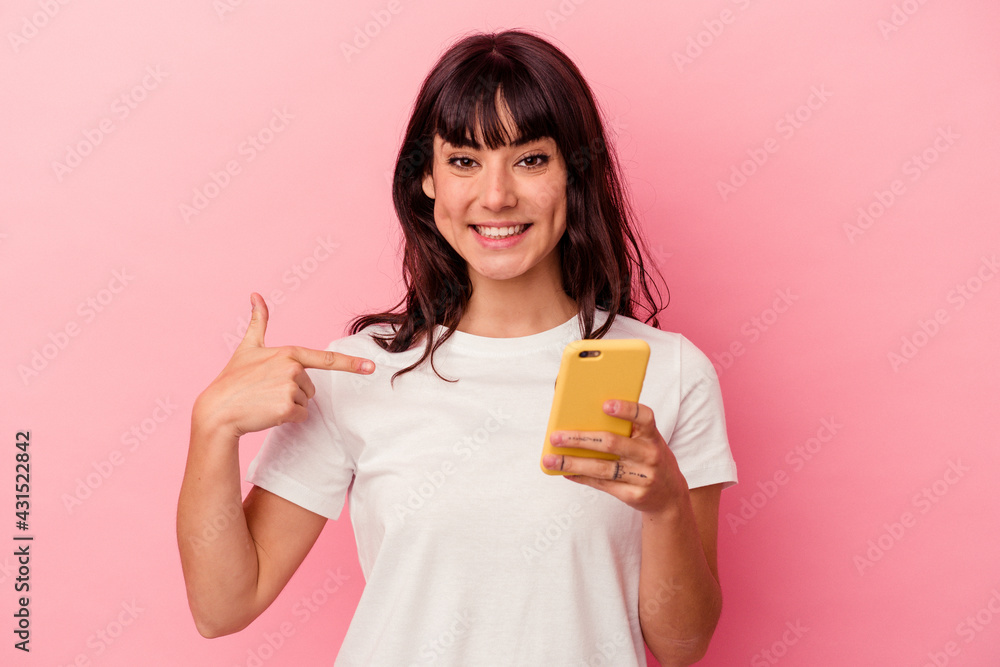 Young caucasian woman holding a mobile phone isolated on pink background person pointing by hand to a shirt copy space, proud and confident Young caucasian woman holding a mobile phone isolated on pink background person pointing by hand to a shirt copy space, proud and confident