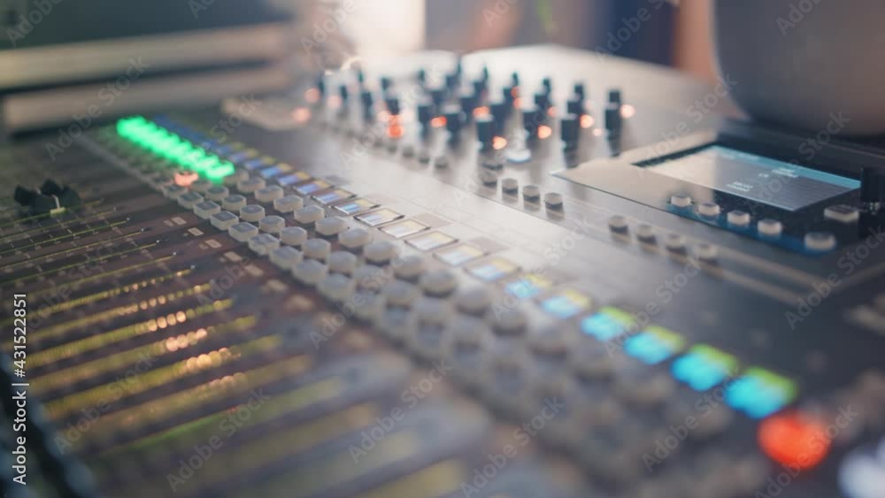 Professional audio recording mixing console with faders and illuminated knobs and buttons and an lcd screen during a recording session. Smooth pan sliding shot in 4K; Shallow depth of Field. Professional audio recording mixing console with faders and illuminated knobs and buttons and an lcd screen during a recording session. Smooth pan sliding shot in 4K; Shallow depth of Field.