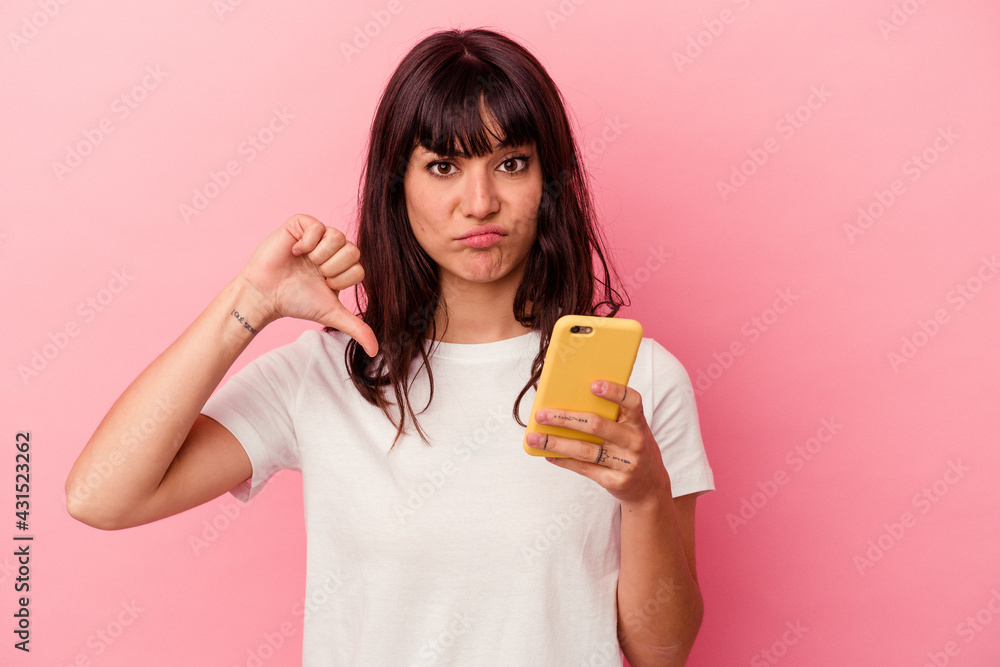 Young caucasian woman holding a mobile phone isolated on pink background showing a dislike gesture, thumbs down. Disagreement concept. Young caucasian woman holding a mobile phone isolated on pink background showing a dislike gesture, thumbs down. Disagreement concept.