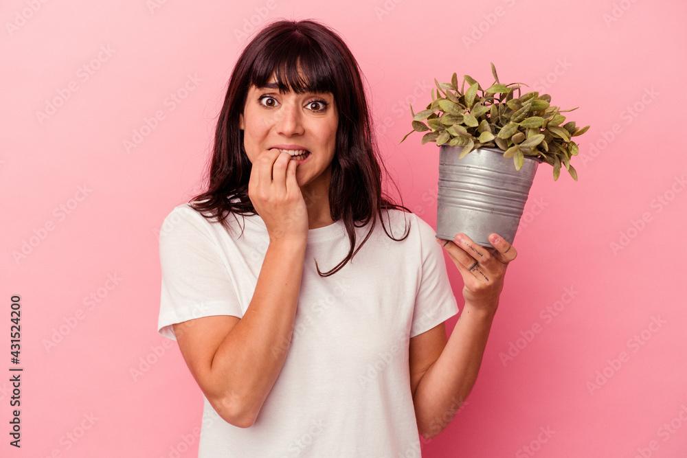 Young caucasian woman holding a plant isolated on pink background biting fingernails, nervous and very anxious. Young caucasian woman holding a plant isolated on pink background biting fingernails, nervous and very anxious.