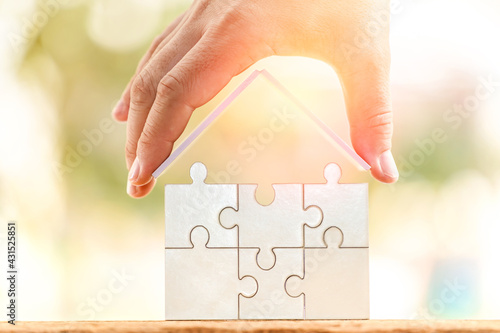 Businessman hand hold a roof connect to jigsaw puzzle a house shape puzzle  in the public park, Business investment or loan for real estate concept.