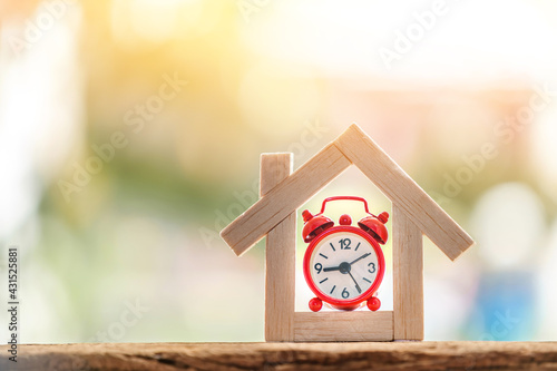 Home model and alarm clock put on the wood on sunlight in the public park, for buying or installment with real estate concept.