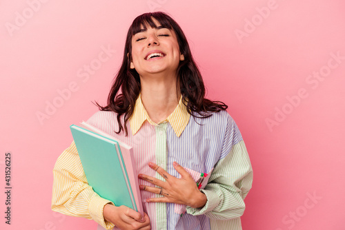 Young student caucasian woman holding books isolated on pink background laughs out loudly keeping hand on chest.