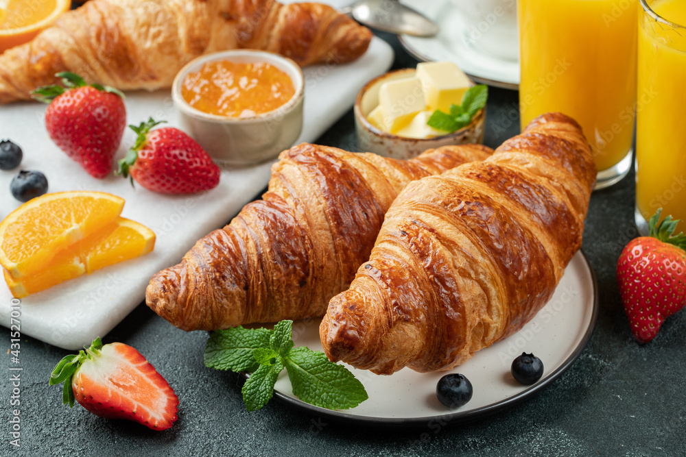 Fresh sweet croissants with butter and orange jam for breakfast. Continental breakfast on a black concrete table.