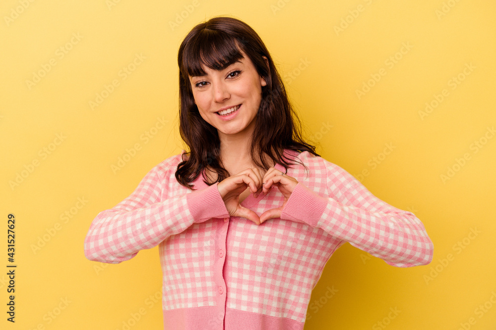 Young caucasian woman isolated on yellow background smiling and showing a heart shape with hands. Young caucasian woman isolated on yellow background smiling and showing a heart shape with hands.