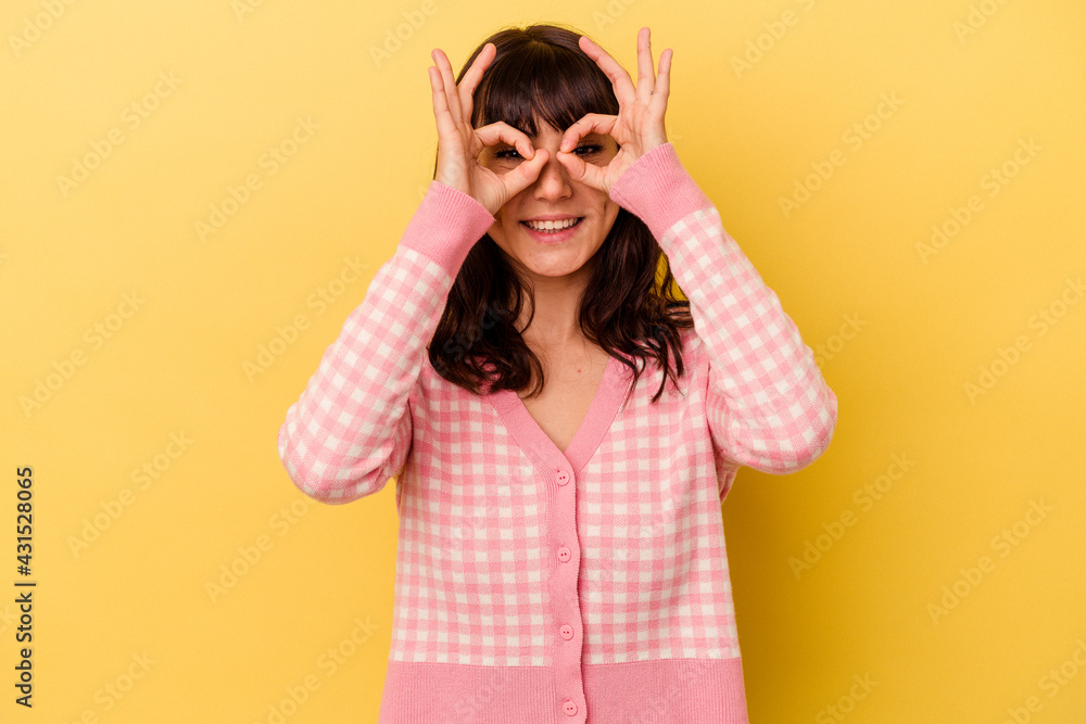 Young caucasian woman isolated on yellow background showing okay sign over eyes Young caucasian woman isolated on yellow background showing okay sign over eyes