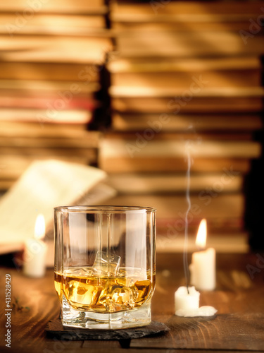 A glass of whiskey on the table with books and burning candles. Copy space  vertical photo.