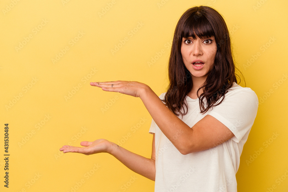Young caucasian woman isolated on yellow background shocked and amazed holding a copy space between hands. Young caucasian woman isolated on yellow background shocked and amazed holding a copy space between hands.